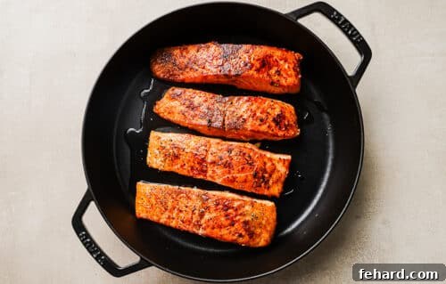 Seared salmon fillets cooking in a cast-iron skillet.