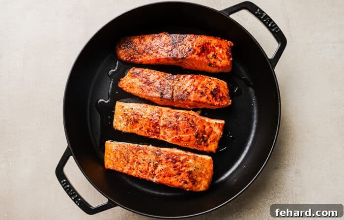 Seared salmon fillets cooking in a cast-iron skillet.