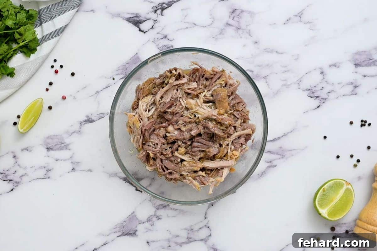 Perfectly shredded pork shoulder piled high in a large mixing bowl, showcasing its tender texture and readiness for the next step.