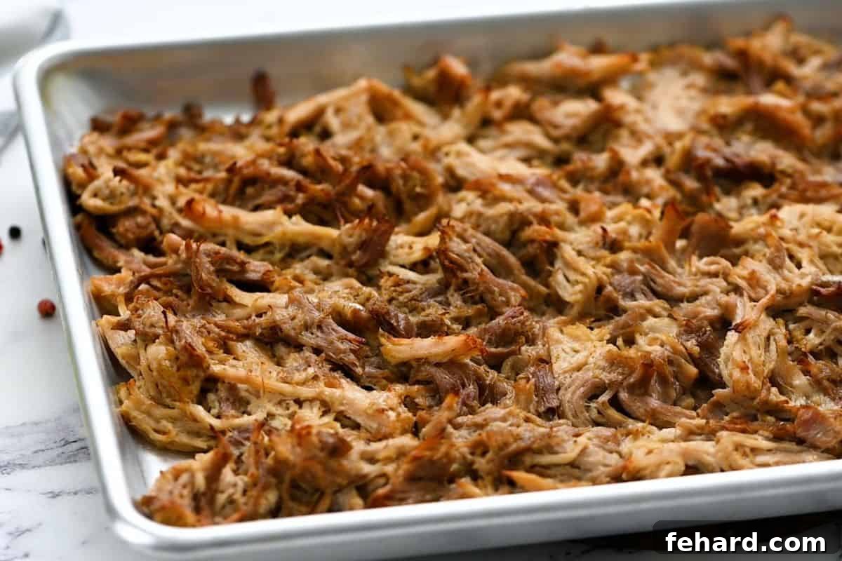 Perfectly crispy, golden-brown shredded pork carnitas spread on a rimmed sheet pan after broiling, showcasing the irresistible charred edges.