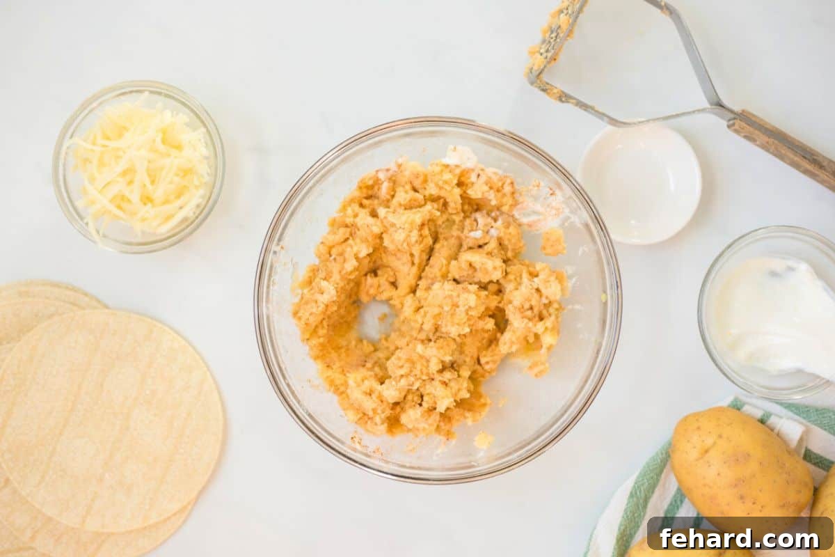 Cheesy Crispy Potato Tacos Mashed Yukon gold potatoes in mixing bowl seasoned with taco seasoning and sour cream.