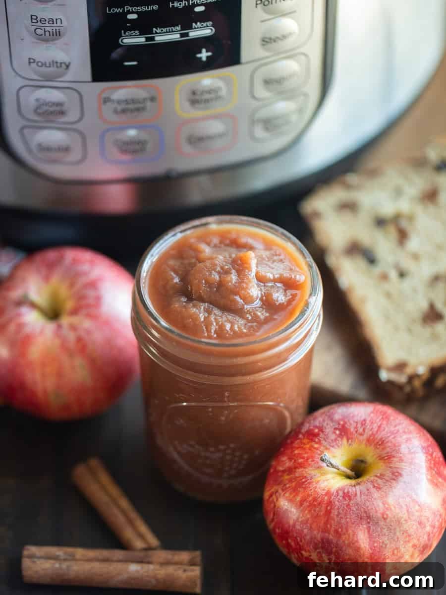 Instant Pot Apple Butter Jar of Instant Pot Apple Butter next to an Instant Pot, fresh apples, and cinnamon sticks, highlighting the rich, thick texture.
