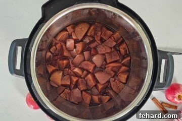 Cooked apples in inner pot of pressure cooker next to fresh apples and cinnamon sticks.