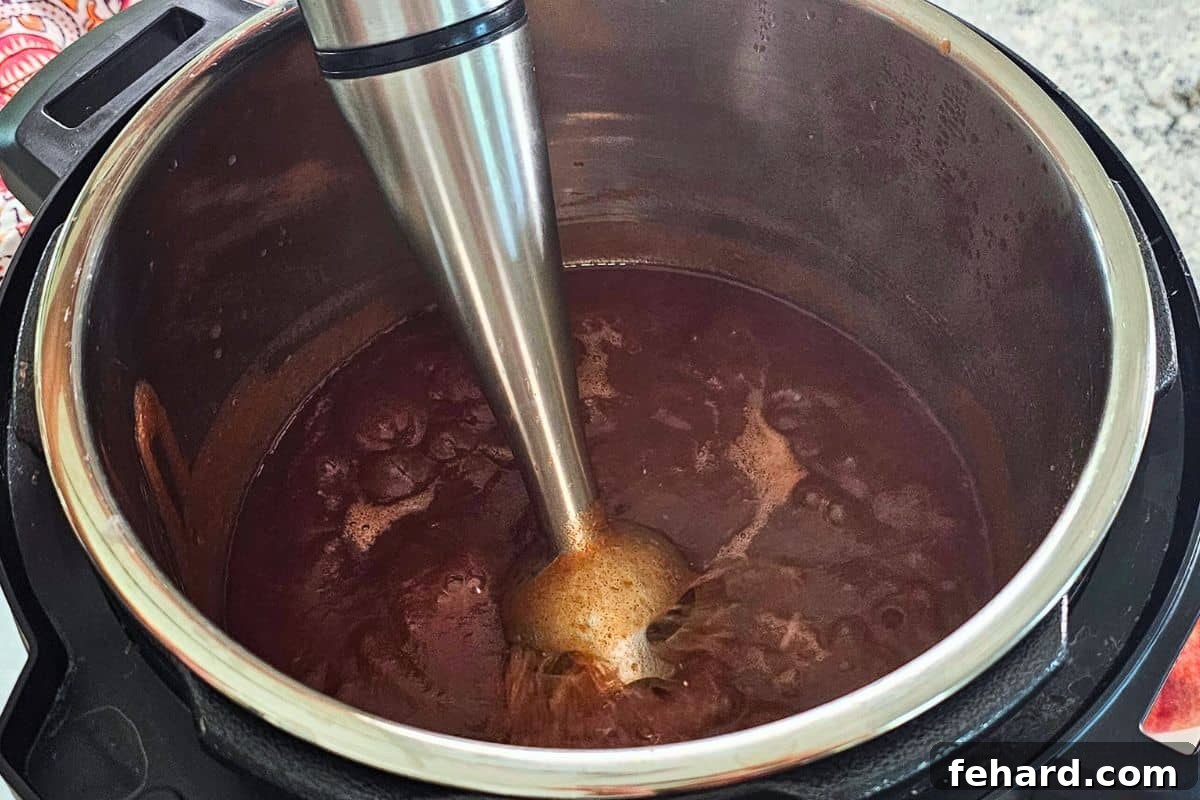 Easy Apple Butter Recipe An immersion blender inside the inner pot, actively blending cooked apples into smooth apple butter.
