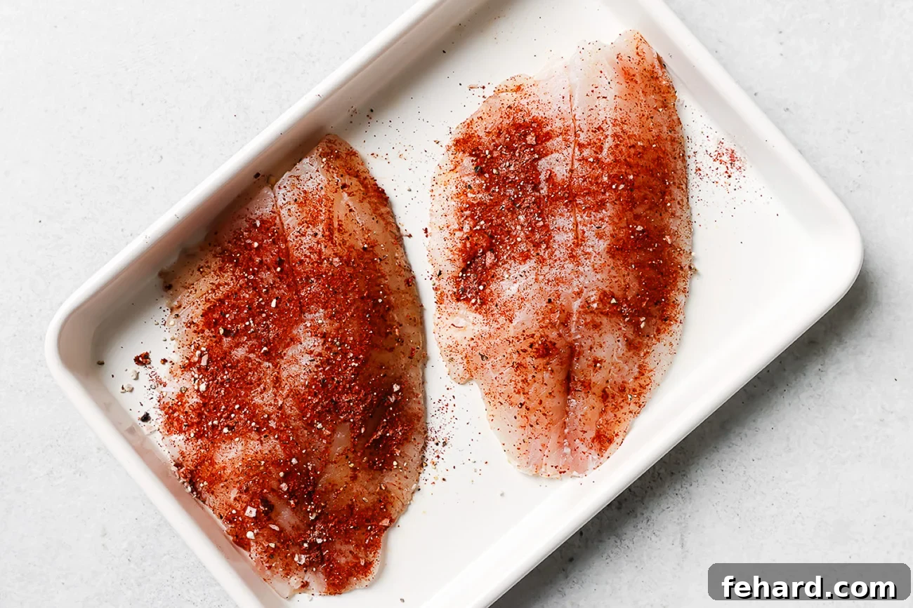 Seasoned raw tilapia fillet on a white baking sheet.
