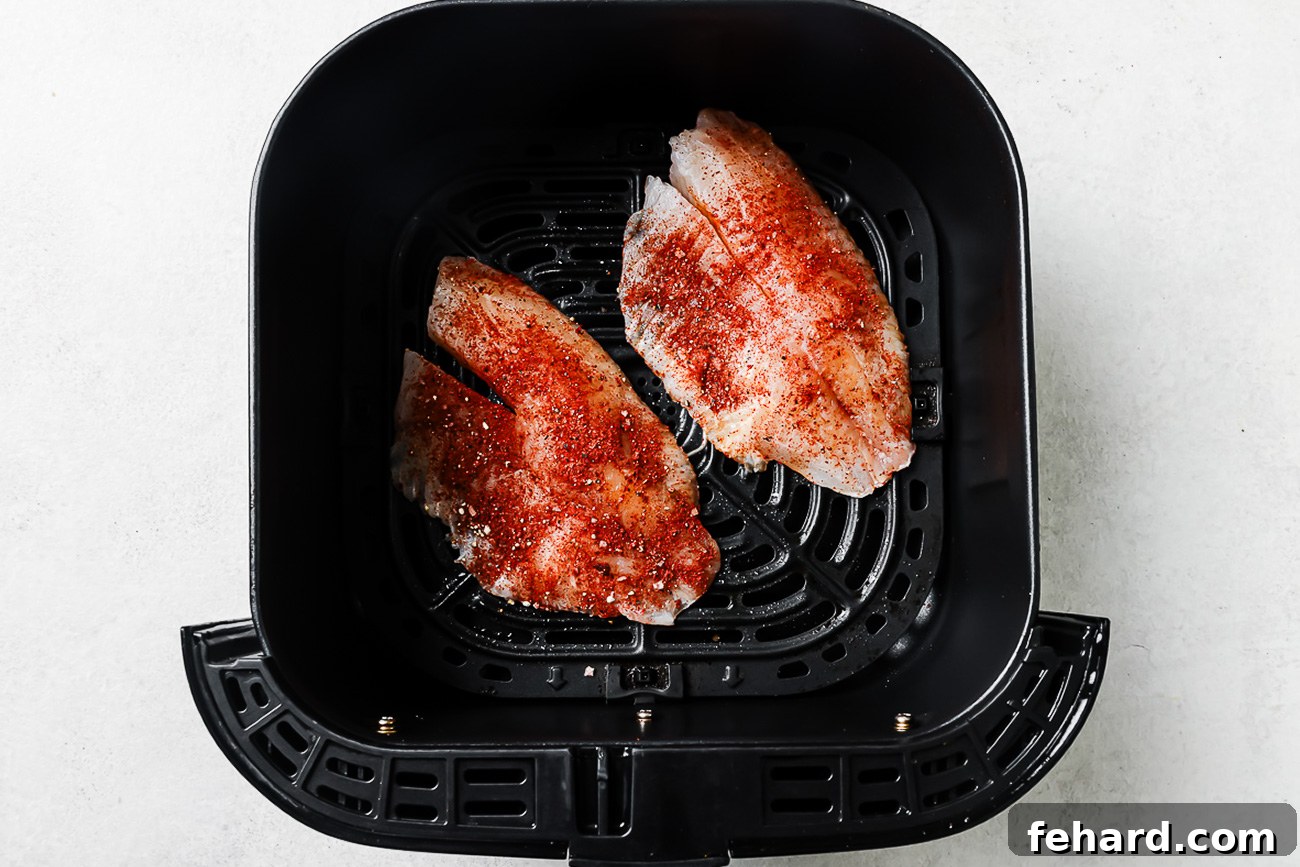 Seasoned raw tilapia in an air fryer basket.