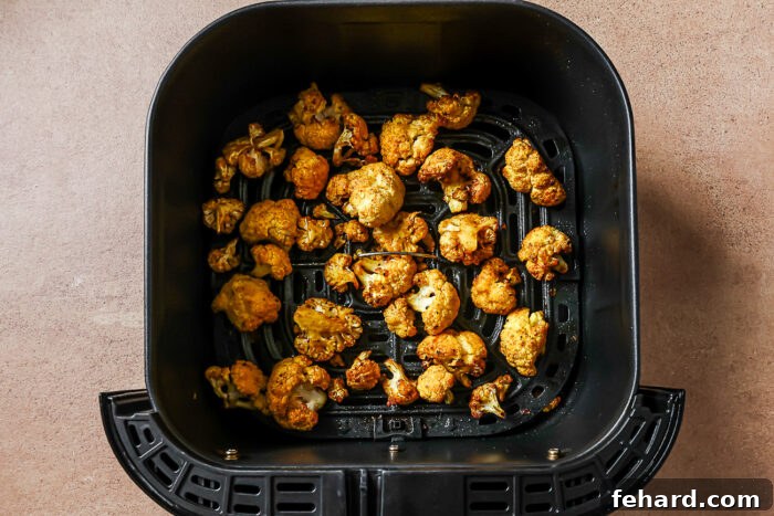 Overhead view of seasoned cooked cauliflower florets in an air fryer basket.