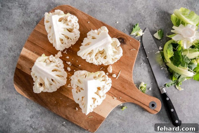 Cauliflower head cut into four parts on a wooden board.