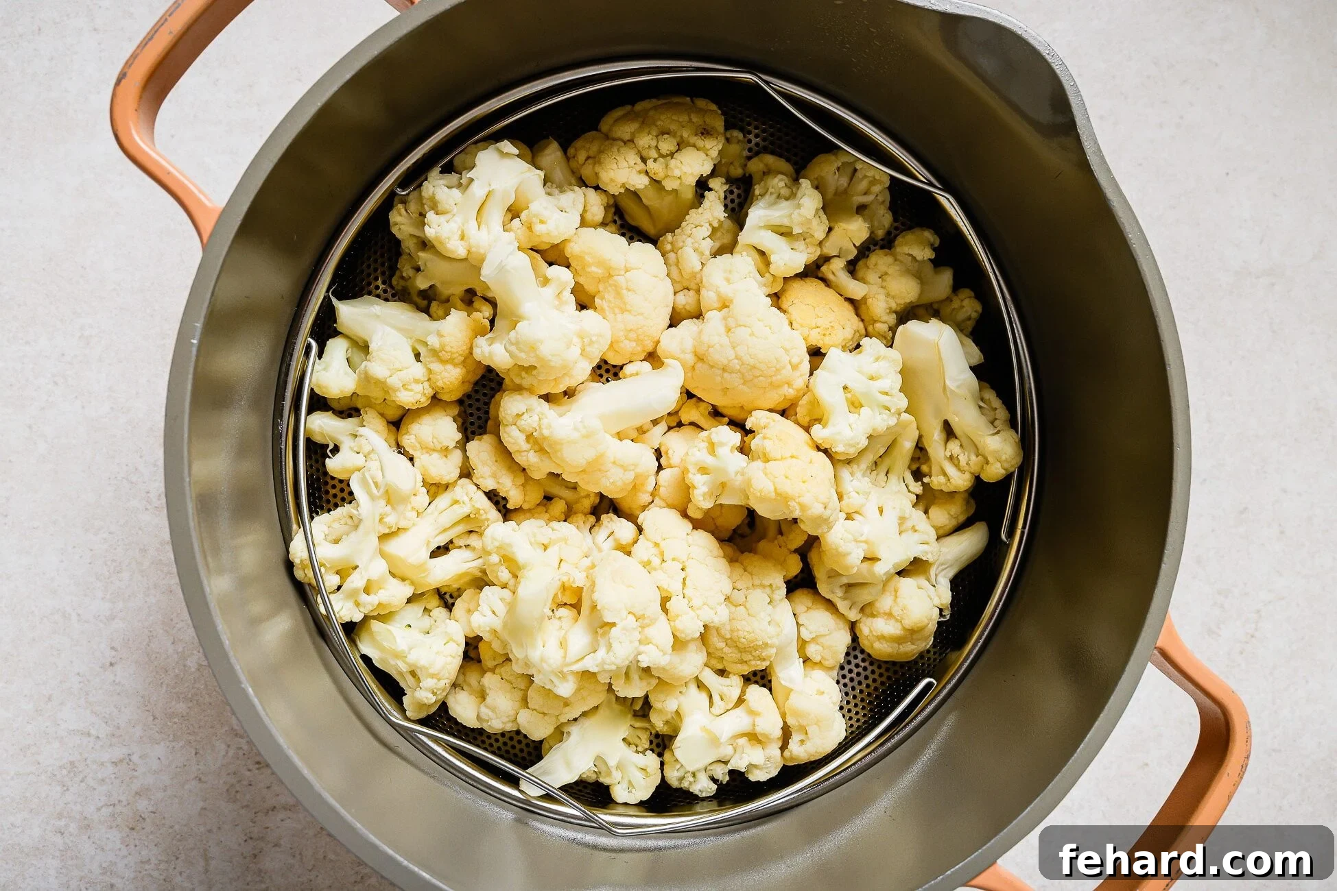 Cauliflower florets in a steamer basket inside a pot.