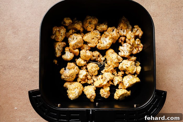 Overhead view of seasoned cauliflower florets in an air fryer basket.