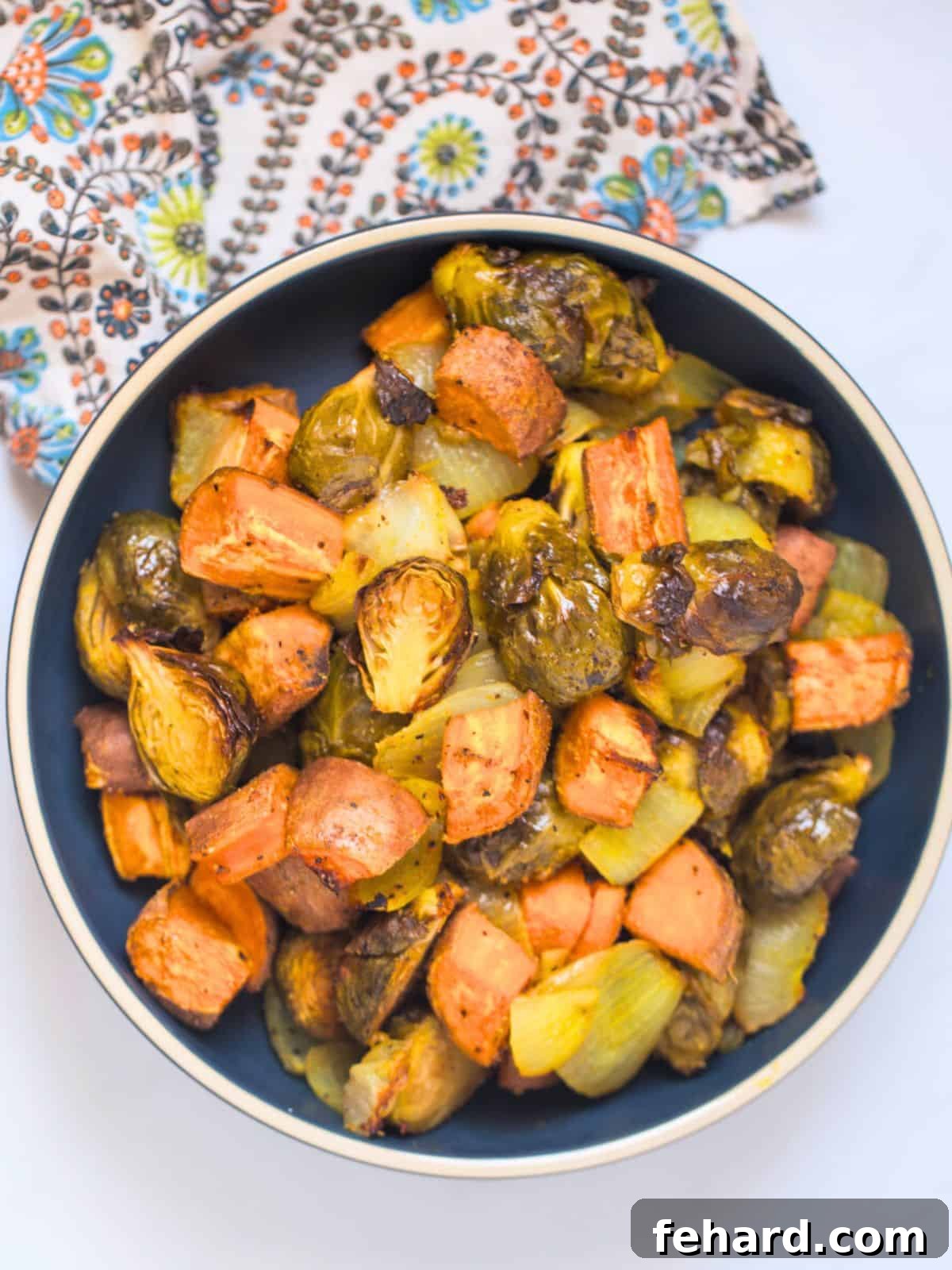 Roasted Fall Vegetables Side Dish A rustic blue bowl filled with golden-brown roasted fall vegetables, including caramelized Brussels sprouts, sweet potatoes, and onions, garnished with fresh herbs.
