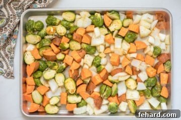 Seasoned Brussels sprouts, sweet potatoes, and onions on rimmed sheet pan.