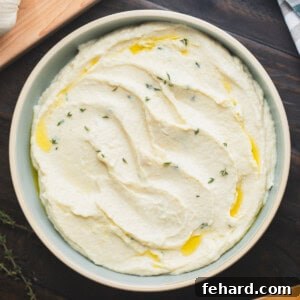 Bowl of creamy parsnip puree with horseradish topped with a bit of olive oil and fresh thyme leaves.