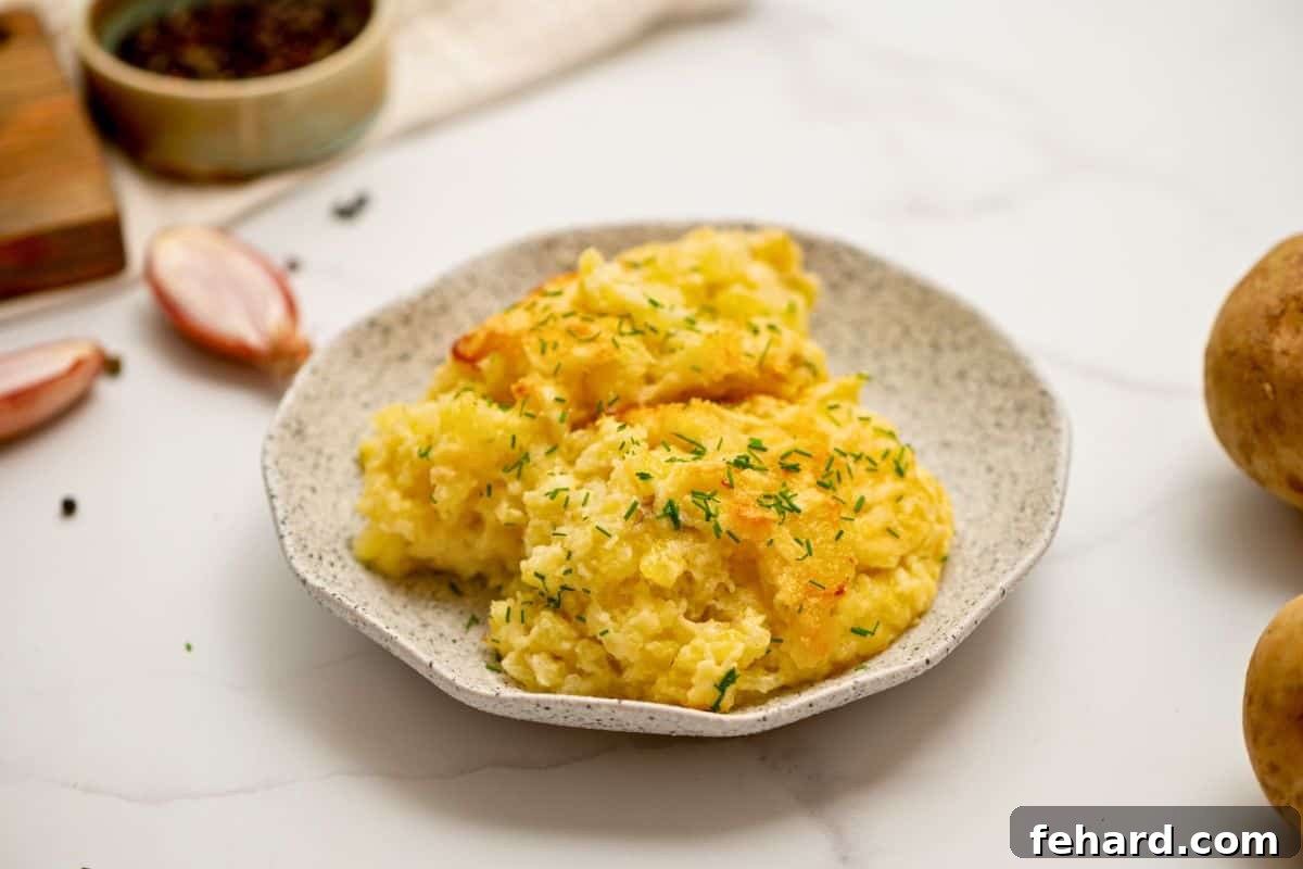 Cheesy Potato Romanoff Serving A generous serving of creamy, cheesy Potatoes Romanoff on an elegant gray plate, topped with a vibrant sprinkle of fresh minced chives.
