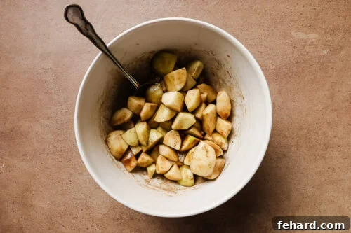 Diced and peeled apples mixed with warm spices in a white bowl, ready for baking.