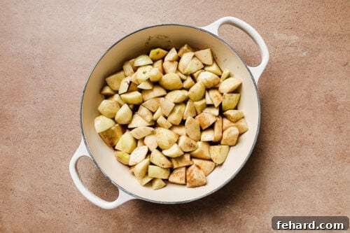 Diced and peeled apples mixed with warm spices in a white skillet, ready for baking.