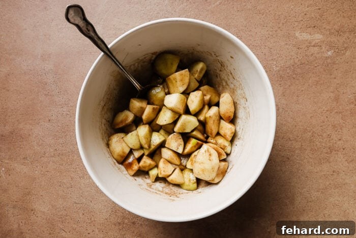 Warm Spiced Gluten Free Apple Crumble 4 Diced and peeled apples mixed with warm spices in a white bowl, ready for baking.