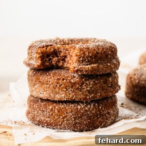Close-up of three stacked donuts, with the top donut showing a bite taken out, on a wooden surface.