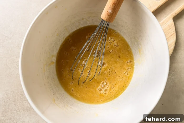 Wet baking ingredients inside a mixing bowl, including eggs, sugar, melted butter, almond milk, vanilla, and reduced apple cider.