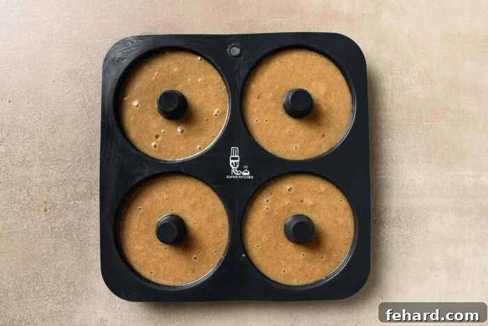 Donut batter piped into a donut baking pan, filling each cavity about three-quarters full.