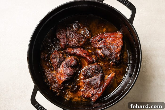 overhead view of apple cider braised pork shoulder in a black Dutch oven pot.