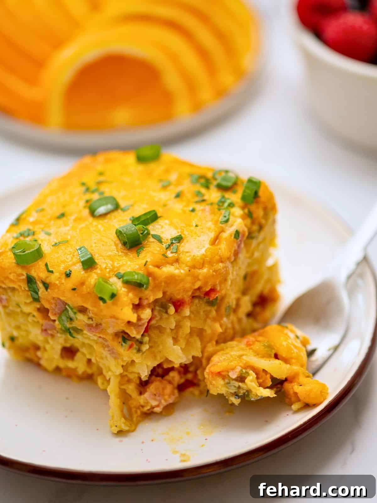 Hearty Crockpot Breakfast Casserole A perfectly sliced piece of Crockpot Breakfast Casserole with visible layers of golden-brown hash browns, diced ham, fluffy eggs, and melted cheddar cheese, garnished with fresh green onions, on a white plate.