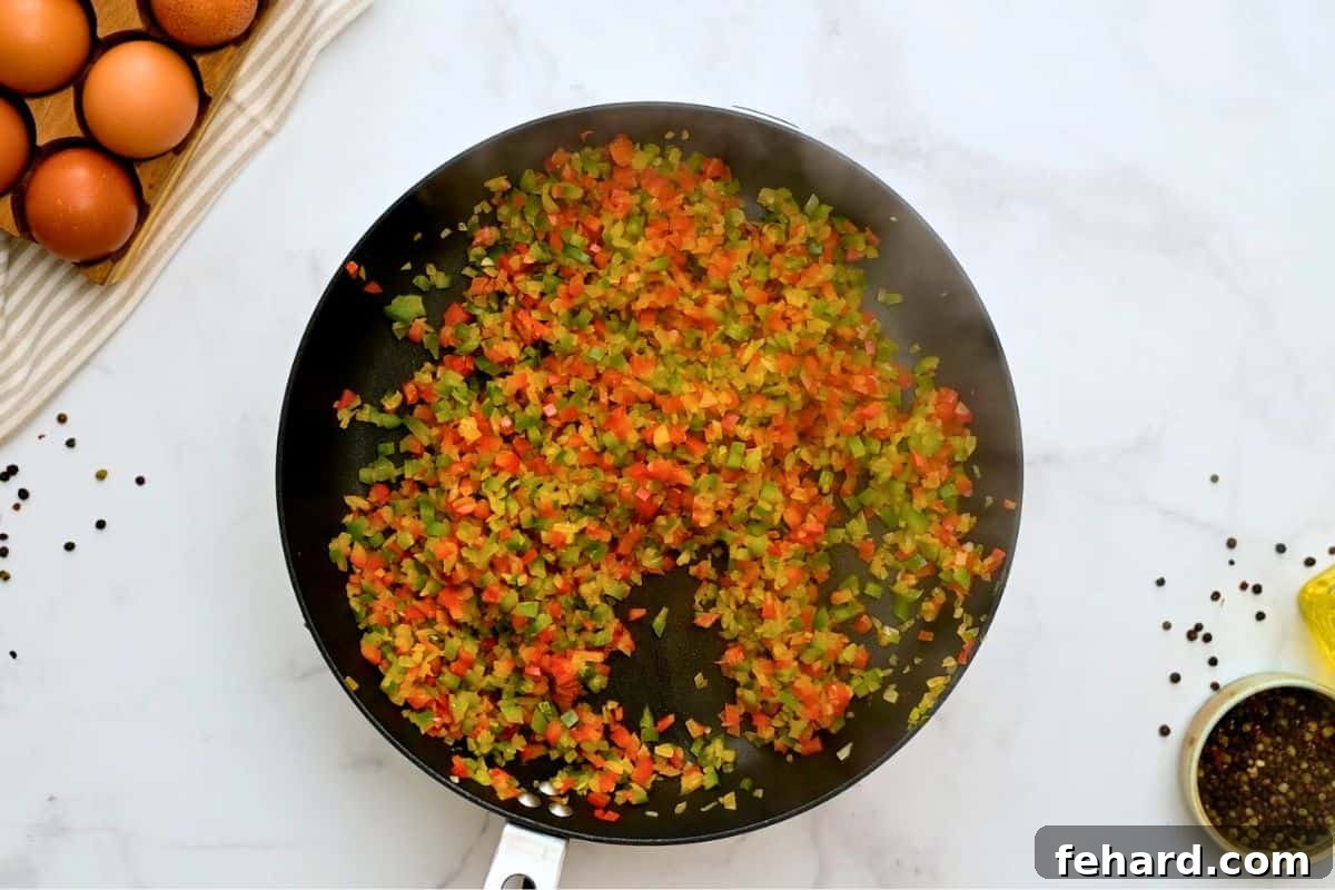 Sautéed Peppers and Onions Diced red and green bell peppers and onions sizzling in a large nonstick skillet after being sautéed, ready for the slow cooker breakfast casserole.