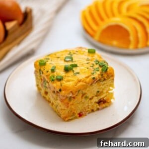 Slice of crockpot breakfast casserole with hashbrowns, ham, and cheese on plate topped with sliced green onions.