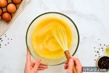 Lazy Day Breakfast Bake 4 Mixing bowl with 12 eggs and milk being whisked by hand for egg casserole.