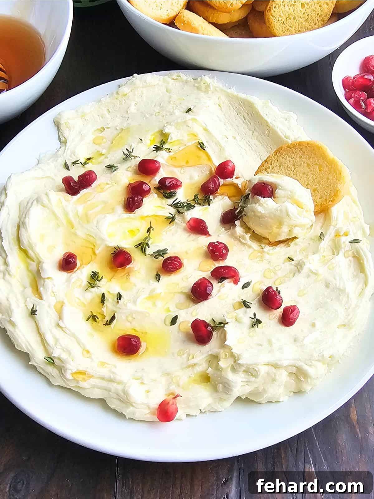 Whipped Brie Whipped brie cheese spread out in white serving dish topped with honey, thyme leaves, pomegranate seeds, and olive oil served with crostini on the side.