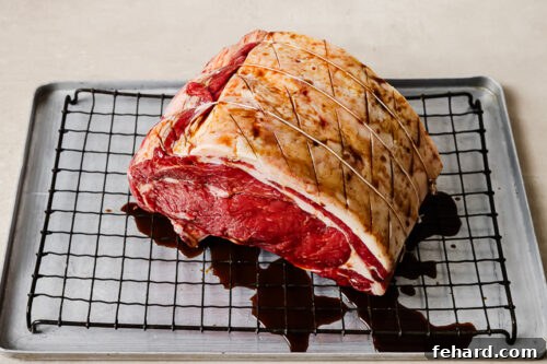 Raw prime rib roast on a wire rack being coated with Worcestershire sauce for the reverse sear prime rib recipe.