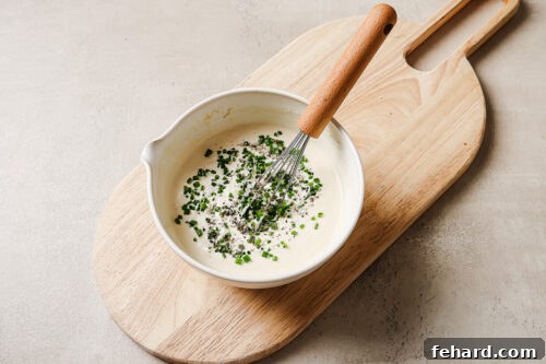horseradish sauce in a white bowl with chives on a wooden board.