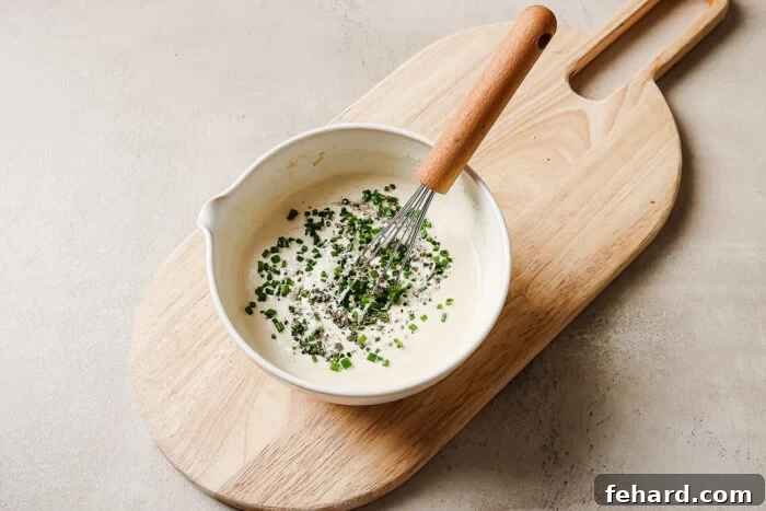 horseradish sauce in a white bowl with chives on a wooden board.