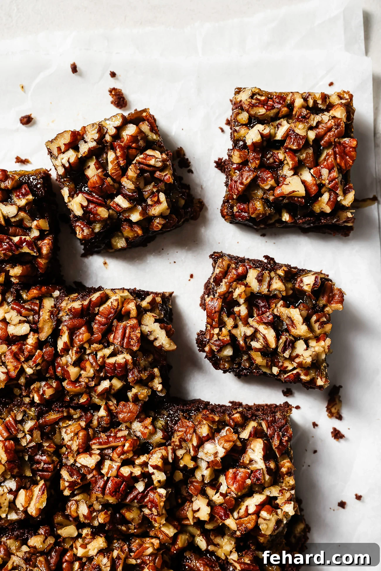 Pecan Pie Swirl Brownies 2 Overhead view of pecan pie brownies cut into squares on parchment paper, featuring a gooey chocolate base and caramelized pecan topping.