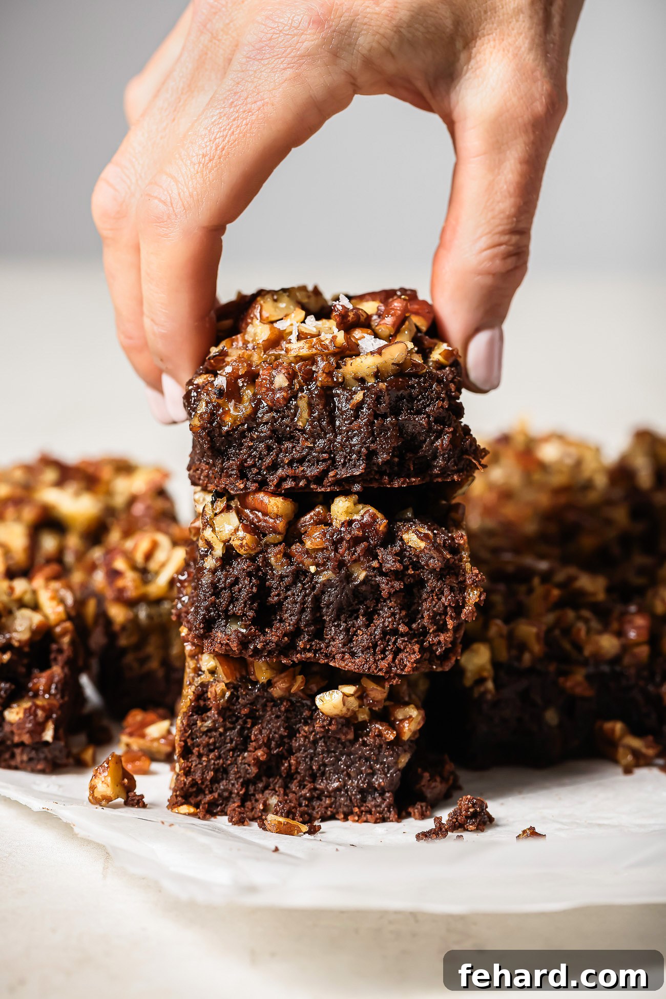 Pecan Pie Swirl Brownies 11 Hand holding a stack of gooey pecan pie brownies with a rich chocolate base and caramelized pecan topping.