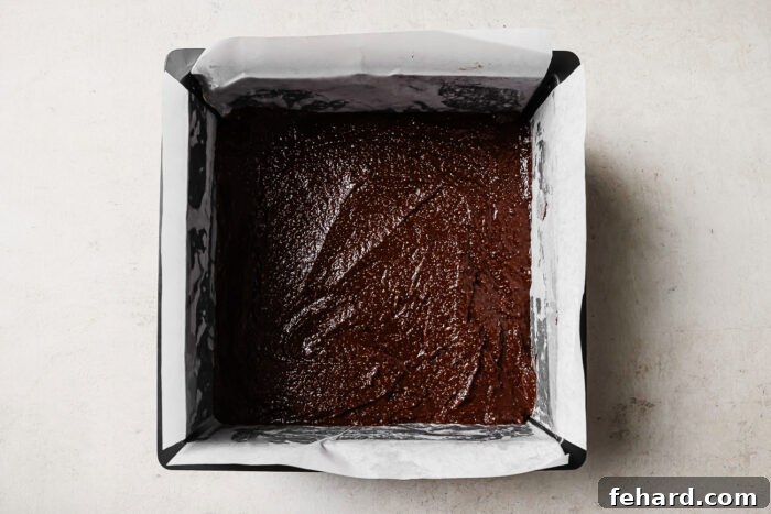 Pecan Pie Swirl Brownies 6 Chocolate brownie batter evenly spread in a parchment-lined square baking pan, ready to bake.
