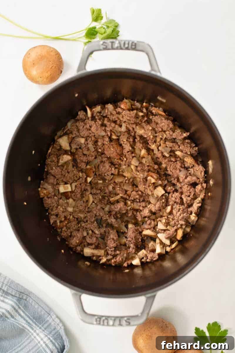Ground beef with minced yellow onion, mushrooms, and garlic sauteed in large pot for beef stroganoff.