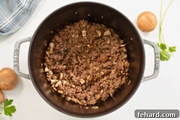 Ground beef with minced yellow onion, mushrooms, and garlic sauteed in large pot for beef stroganoff.