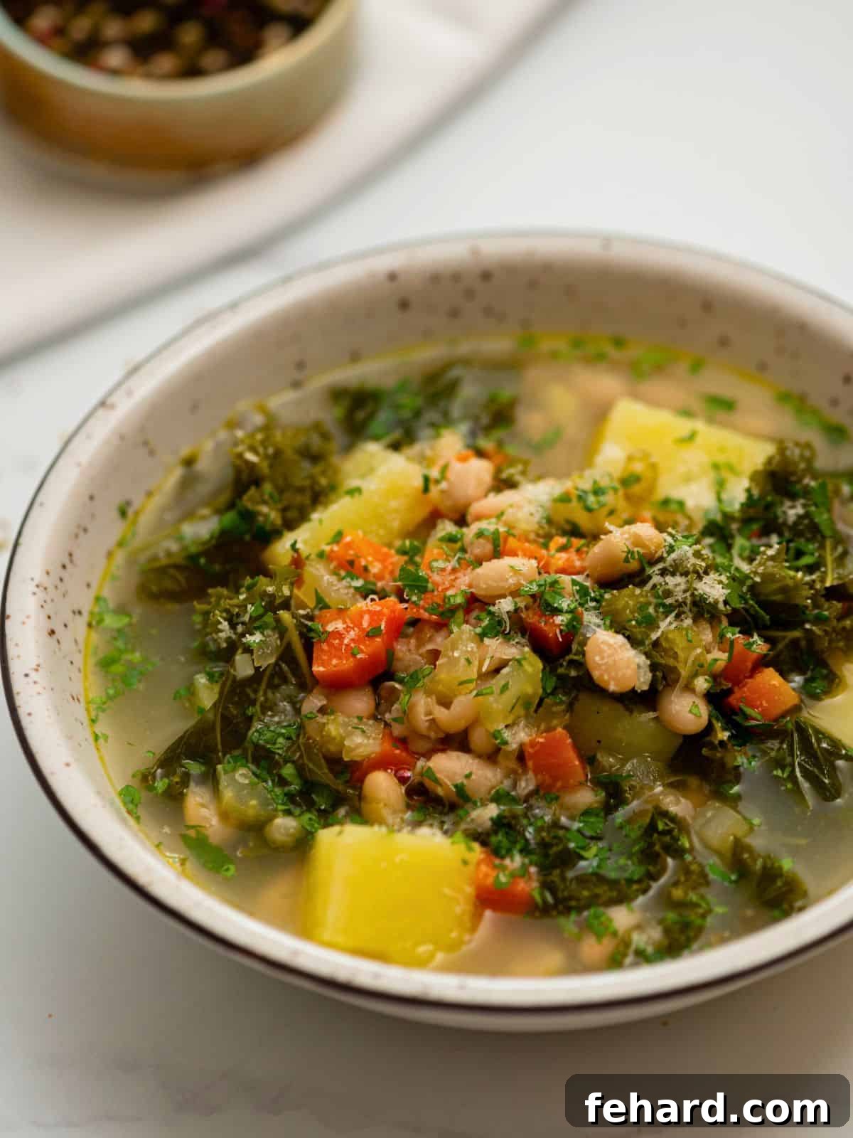 A steaming bowl of homemade white bean soup with vibrant kale, garnished with a sprinkle of grated Parmesan cheese and fresh parsley.