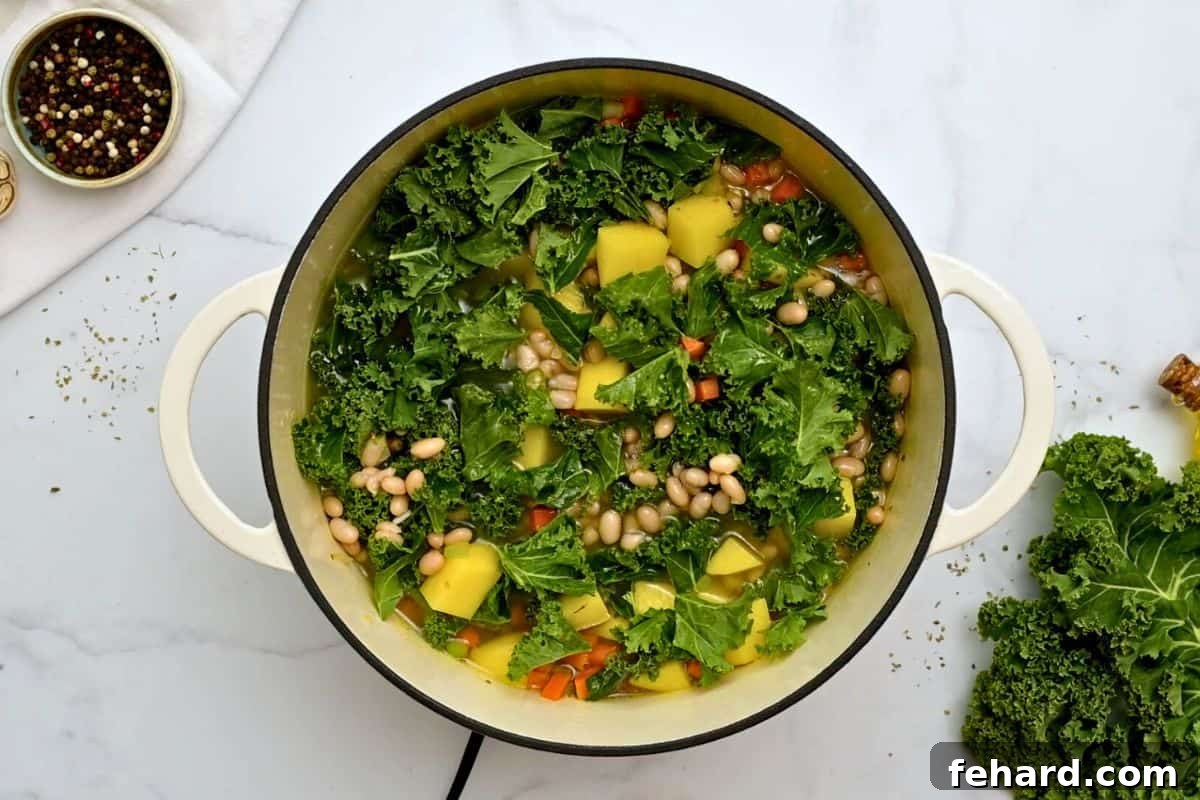 Freshly chopped kale and diced potatoes being added to a simmering pot of broth and aromatics to make white bean soup.