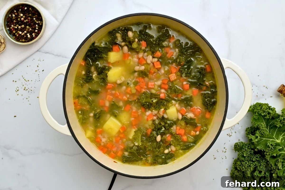 A large soup pan filled with fully cooked white bean and kale soup, after simmering, showing tender vegetables and a rich broth.