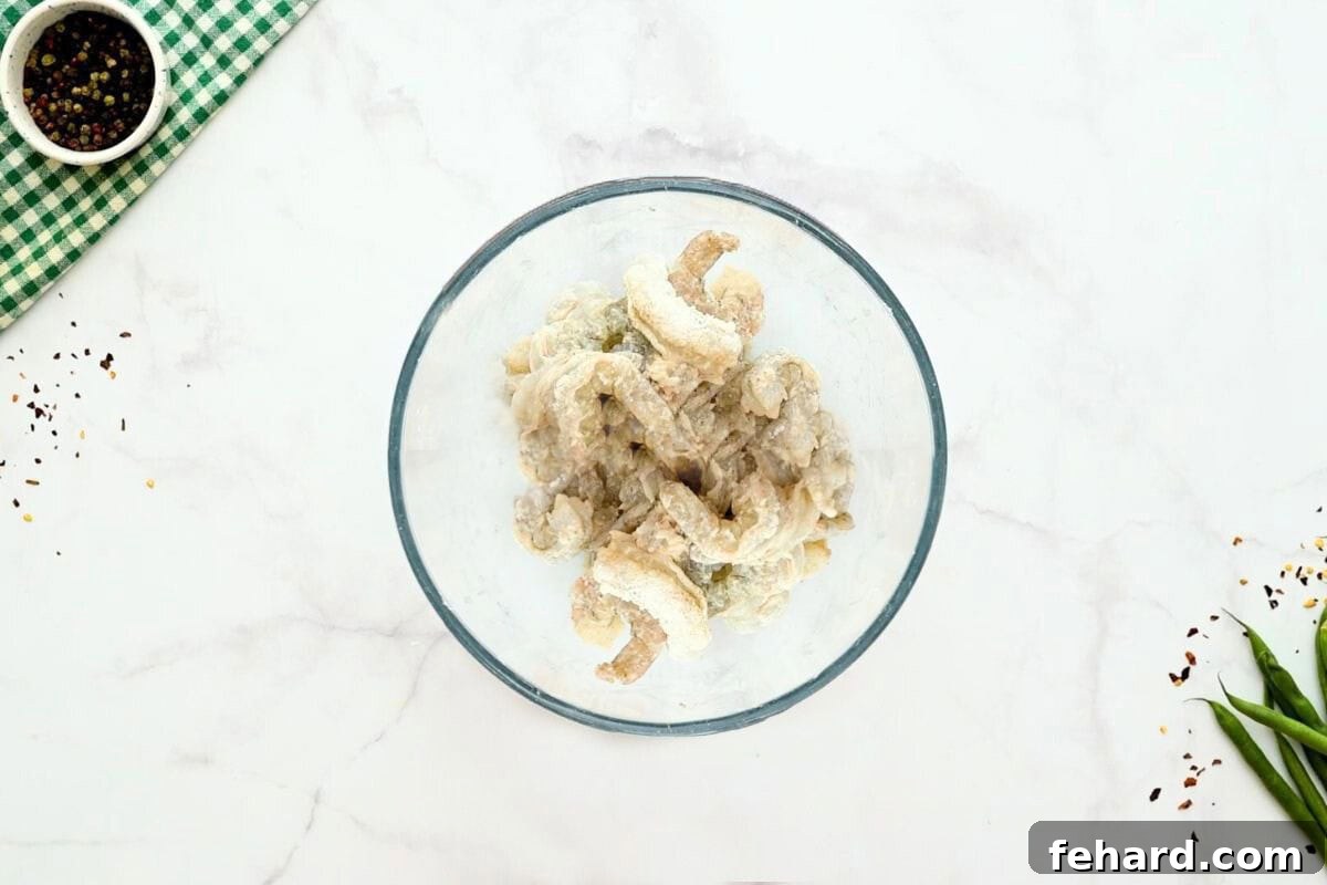 Raw shrimp coated evenly in cornstarch, salt, and pepper, meticulously prepared and ready for immediate pan-frying.