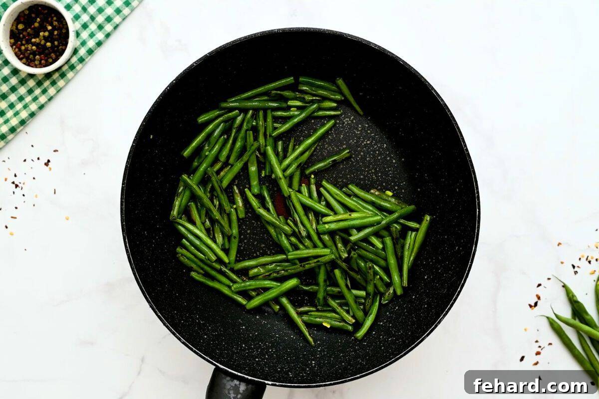 Vibrant green beans, perfectly crisp-tender and lightly browned, being stir-fried in a large skillet for the homemade Hunan Shrimp.