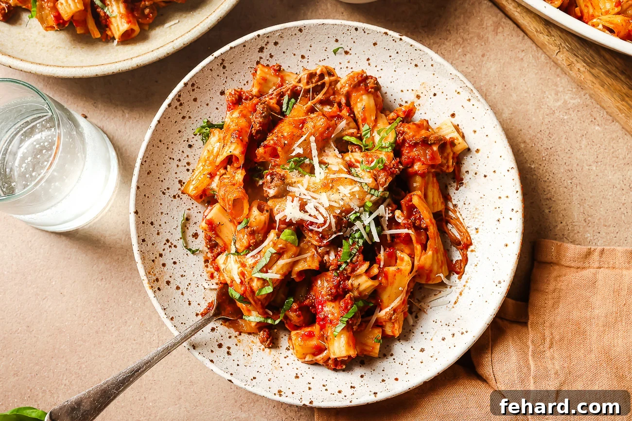 Overhead view of a serving of baked rigatoni with ground beef on a white plate, garnished with fresh basil, showcasing the rich sauce and melted cheese.