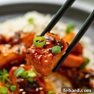 A salmon bite richly coated in a sticky honey soy glaze, being delicately picked up with chopsticks, against a blurred background.