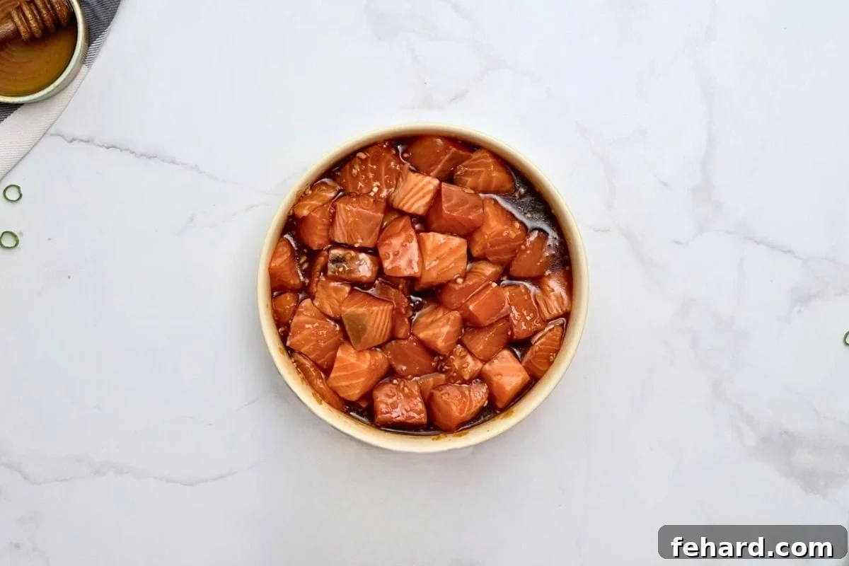 Perfectly cut salmon cubes luxuriating in a honey soy marinade within a shallow dish, ready for cooking.