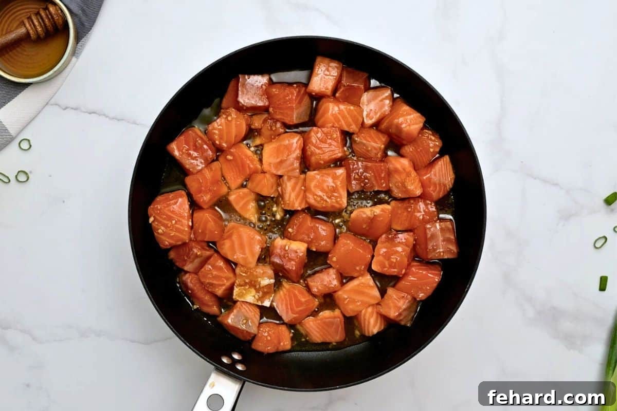 Cubed marinated salmon arranged in a single layer in a hot skillet, beginning to develop a beautiful sear.