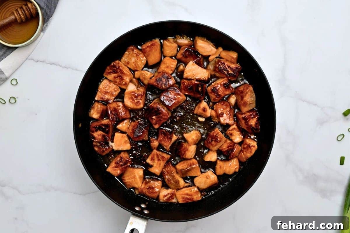 Perfectly seared, golden-brown salmon bites in a single layer within a skillet, showcasing their delicious crust.