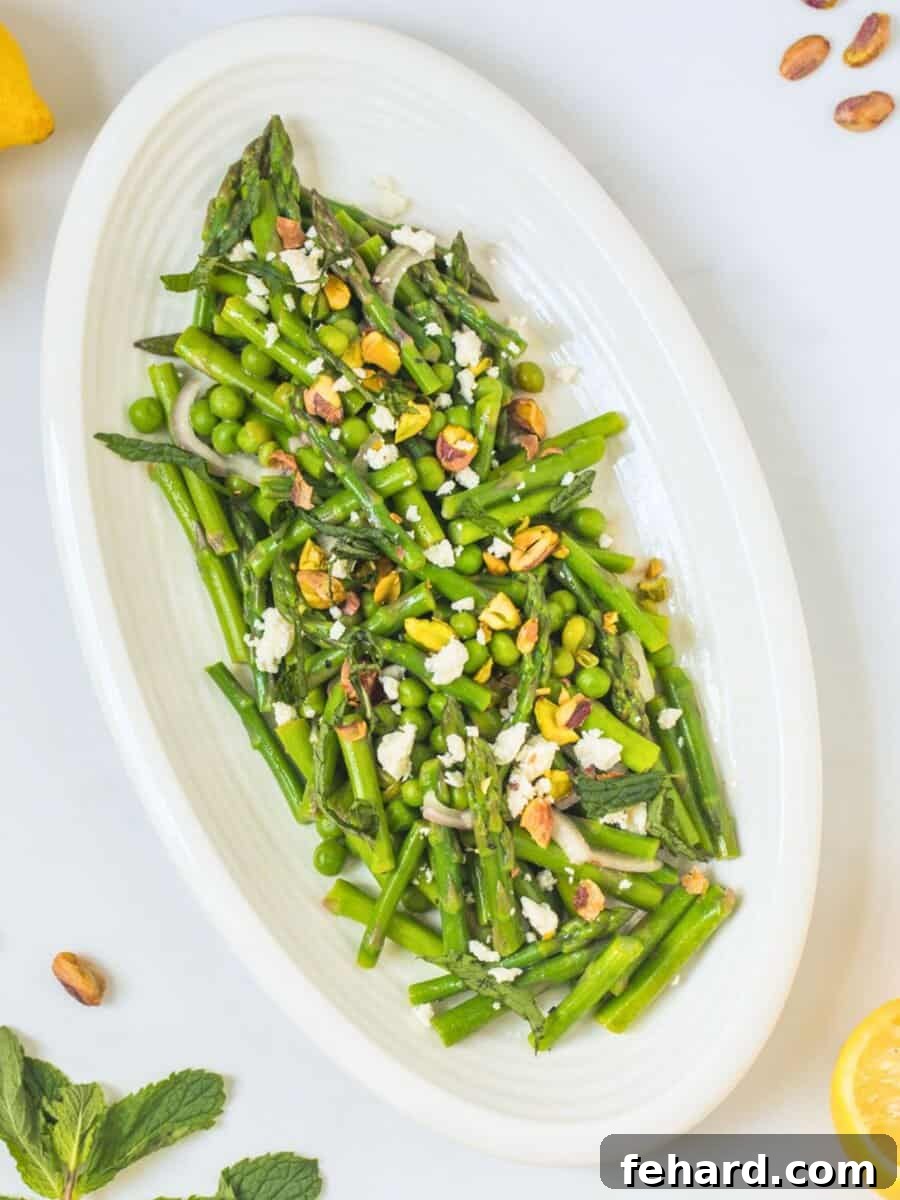 A vibrant Asparagus Salad dressed with fresh lemons, topped with sweet peas, creamy feta, crunchy pistachios, and fresh mint leaves, elegantly arranged on a serving platter. This image highlights the fresh ingredients and appealing presentation of the salad.
