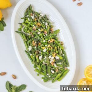 Asparagus salad with peas, feta, pistachios, and mint on platter next to juiced lemons.